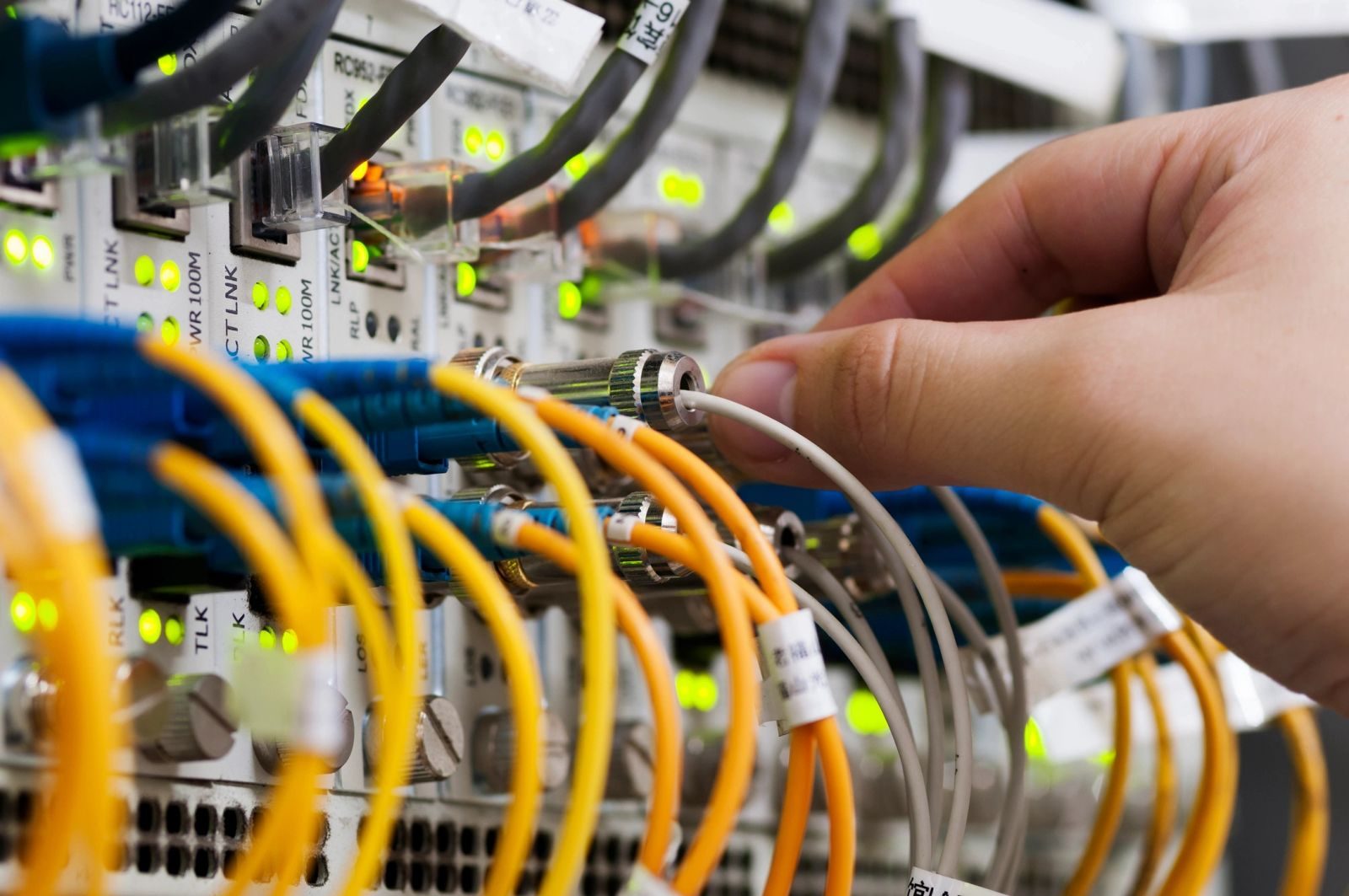 Hand connecting a fiber optic cable to network equipment.