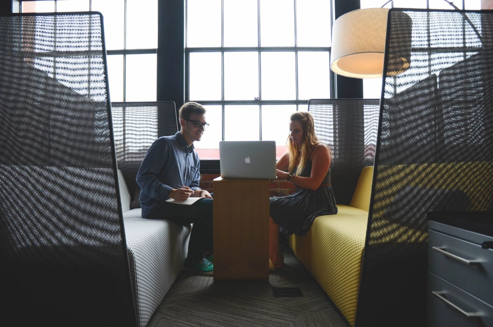 Two people working on a laptop in a cozy office booth.